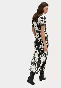 Czarna sukienka w kwiaty z krótkimi rękawami, z białymi kwiatami i koronkowymi akcentami. Płynny krój i detal w postaci rozcięcia z boku, zestawiona z czarnymi botkami.