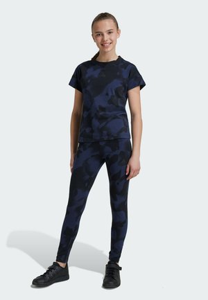 Conjunto de ropa de entrenamiento en camuflaje azul marino, con una camiseta de manga corta y leggings, confeccionado en una tela elástica. Zapatillas deportivas negras completan el look.