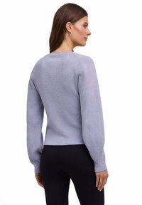 Jasnofioletowy sweter z dzianiny z długimi, lekko bufkami rękawami, prążkowaną fakturą, okrągłym dekoltem i dopasowanym dołem. Noszony z czarnymi legginsami.