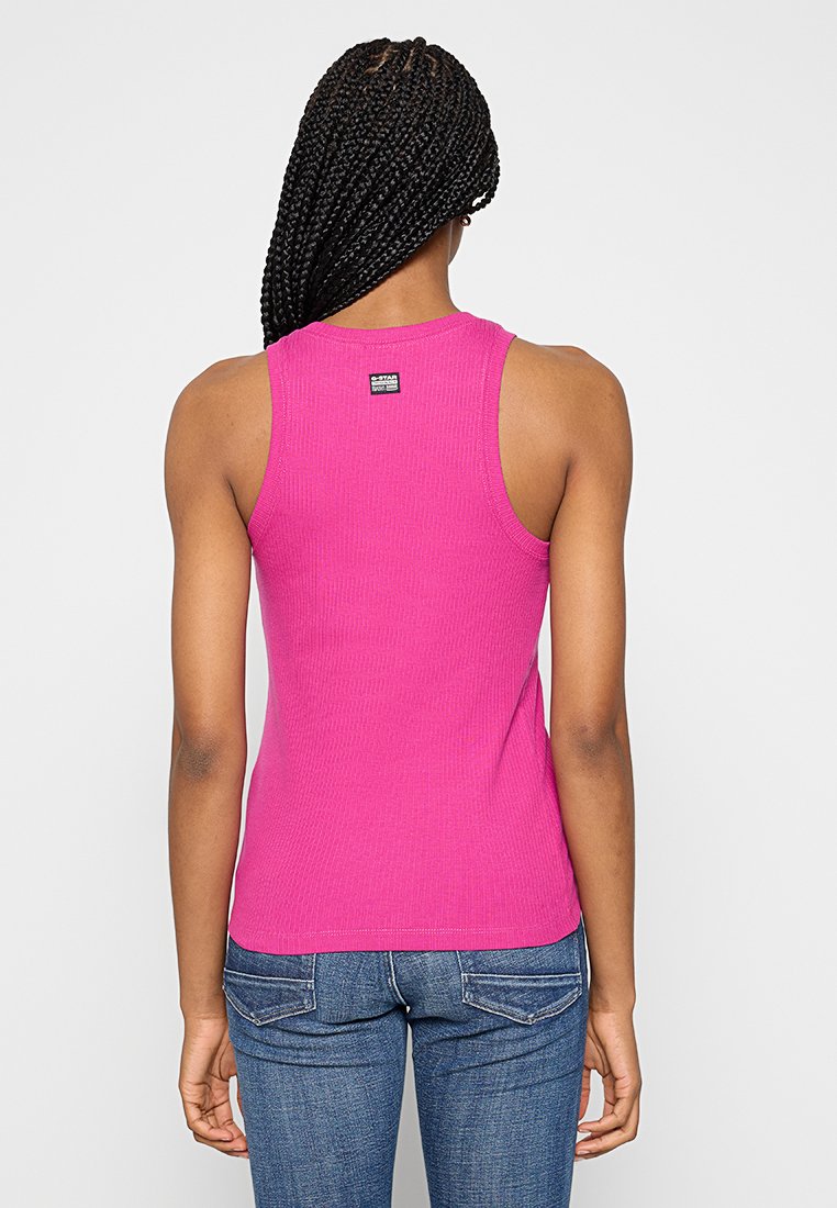 Top aderente e costolato di colore rosa brillante con scollatura rotonda e spalline di media larghezza. Presenta un piccolo etichetta con logo sulla parte posteriore.