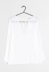 Valkoinen pitkähiha blouse syvällä V-kaula-aukolla, joka on varustettu pitsiyksityiskohdalla. Pehmeä, kevyt kangas, jossa on löysä istuvuus ja kaareva helma. Roikkuu mustassa koukussa.