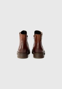 Bottines en cuir marron avec une finition lisse, bout rond, faible talon empilé et coutures décoratives le long de la semelle.