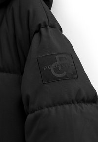 Manga de chaqueta acolchada negra con un parche de logo bordado de POLO CLUB. Tejido texturizado y acolchado con una superficie lisa y un diseño sencillo.