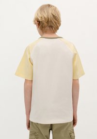 Raglan T-shirt met gele korte mouwen en een crèmekleurig lijf. Heeft een contrasterende groene kraag. De stof lijkt zacht en casual.