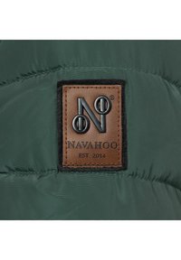 Tela acolchada verde con una etiqueta de cuero marrón que presenta un logotipo en relieve negro con la letra "N" y "NAVAHOO EST 2014." Textura suave con un brillo sutil.