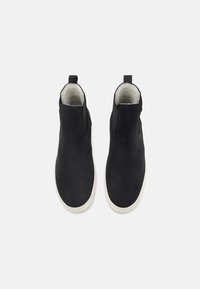 Botas de tobillo de ante negro con paneles laterales elásticos, forro interior crema y suelas de goma blanca. Presenta un lazo para un fácil uso.