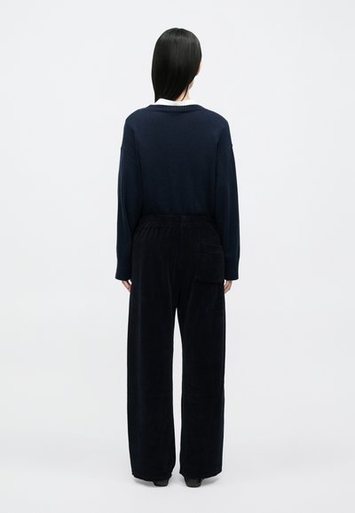 Πλεκτό μπλε ναυτικό πουλόβερ με άνετη εφαρμογή και φαρδύ λαιμόκοψη, συνδυασμένο με μαύρο παντελόνι από κορντόι με φαρδιά μπατζάκια και πλαϊνή τσέπη.