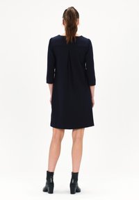 Marineblaue Kleider mit Dreiviertelärmeln, relaxed Fit und einer Rückenfalte. Kombiniert mit schwarzen Stiefeletten. Glatte Textur.