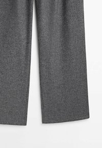 Pantalons larges gris en tissu texturé avec un motif subtil. L'ourlet est droit et la taille est classique sans fermetures visibles.