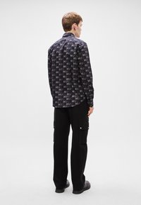 Μαύρο πουκάμισο με επαναλαμβανόμενο σχέδιο κειμένου "HUG", μακριά μανίκια, σχέδιο με κουμπιά. Συνδυάζεται με μαύρες cargo παντελόνες και μαύρες επίπεδες παπούτσια.