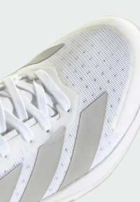 Biele športové topánky s sieťovaným zvrškom, s textúrovanými šedými akcentmi a tromi šedými pruhmi po bokoch. Šnúrky sú ploché a biele.