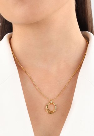 Gouden metalen ketting met onderling verweven ronde schakels aan een delicate ketting, tentoongesteld tegen een lichtgekleurde kraag.