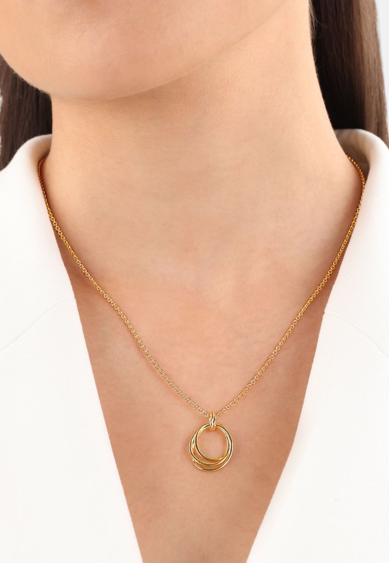 Collana in metallo dorato con anelli circolari intrecciati su una delicata catena, esposta su un colletto di colore chiaro.