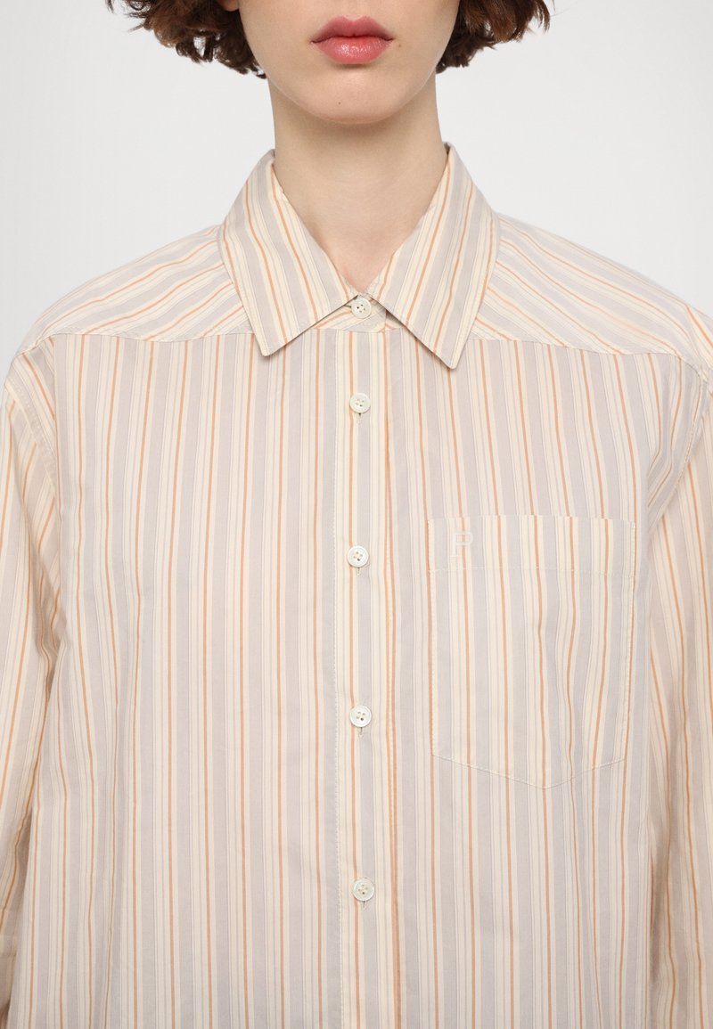 Camisa de botones con rayas verticales en beige claro, naranja pastel y gris. Incluye un bolsillo en el pecho y un collar con puntas. Textura suave.
