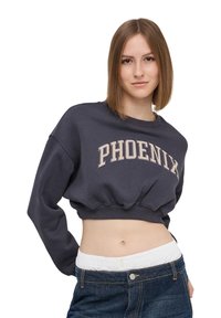 Czarny szary, krótki sweter z napisem "PHOENIX" w jasnobeżowym kolorze, z prążkowanym okrągłym dekoltem i elastycznym wykończeniem. Noszony z dżinsami z wysokim stanem.