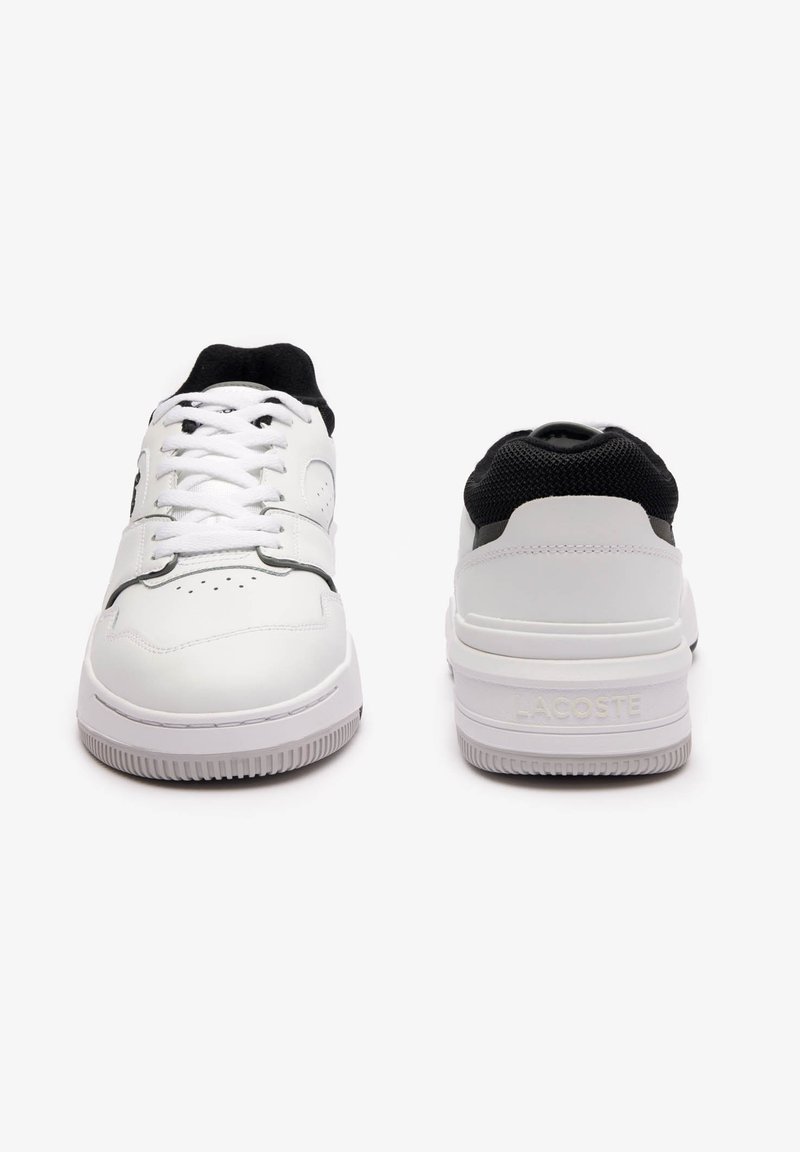 Baskets blanches avec un dessus en cuir lisse et en maille, bout rond, fermeture à lacets, et semelle en caoutchouc texturé avec le logo Lacoste à l'arrière.