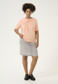 Peachfarvet, kortærmet top med et snoet design foran, parret med en grå denim blyantskirt og sorte platform sko.