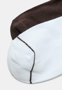 Coppia di calzini di cotone a media altezza, uno bianco con cuciture marroni sulla punta e l'altro completamente marrone, sovrapposti su uno sfondo chiaro.
