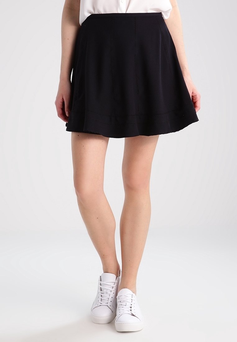 Jupe patineuse noire avec une silhouette évasée, présentant des détails de couture subtils. Associée à des baskets de sport blanches.