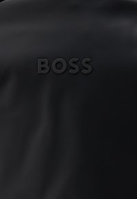 Melnas teksturētas virsmas ar izceltiem melniem burtiem, kas centrā attēlo vārdu "BOSS".