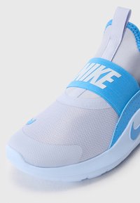Zbliżenie białego i jasnoniebieskiego modelu sneakersów Nike slip-on z siateczkową cholewką, elastycznym paskiem z logo oraz uchwytem na pięcie.
