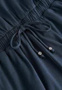 Dunkelblaue Bekleidung mit einem gerafften Bund und einem Kordelzug. Der Kordelzug hat silberne Hardware-Details an den Enden. Weicher Stoff.