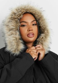 Mustat parka, jossa on tekoturkilla vuorattu huppu. Turkki on vaaleanruskea, tummempiin kärkiin siirtyen. Takissa on vetoketju ja rento leikkaus.