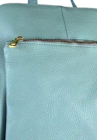 Sac en cuir texturé bleu clair avec une poche zippée à l'avant dotée d'une tirette dorée et d'une anse assortie.