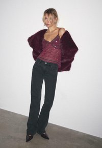 Camisola bordeaux con paillettes e spalline sottili, abbinata a uno strato esterno peloso color bordeaux e jeans neri a zampa di elefante. Completato con tacchi neri a punta.
