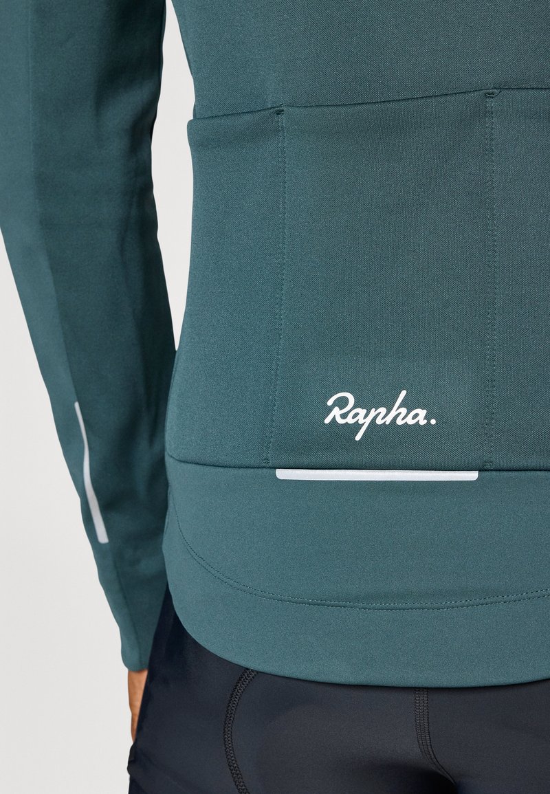 Maglia da ciclismo a maniche lunghe verde con una texture liscia, design aderente e logo bianco sul retro. Presenta dettagli riflettenti per una maggiore visibilità.