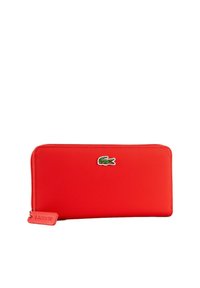 Portefeuille zippé rouge en matière texturée, avec un logo crocodile Lacoste vert et une petite étiquette de marque.