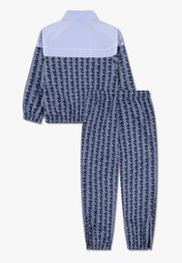 Set trenirk in mornariško modri z geometrijskim belim vzorcem. Ima elastične manšete in svetlo modro ovratnico z zadrgo.