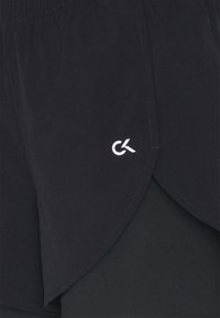 Pantalones cortos deportivos negros con un diseño en capas, dobladillo curvado, textura suave y un acento de logo blanco en la parte delantera.