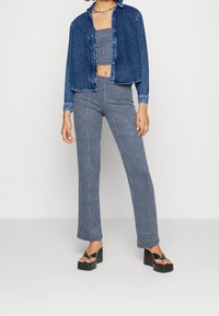 Camicia di denim abbinata a un top bandeau a fantasia e pantaloni a gamba larga. Blu con strisce bianche ondulate. Sandali con plateau neri.