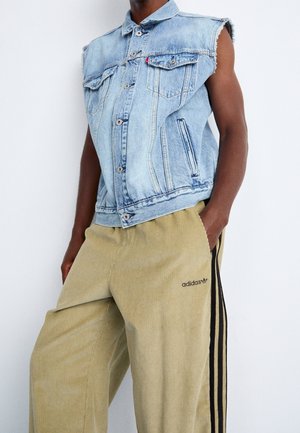 Chaleco sin mangas de mezclilla azul claro combinado con pantalones de pana beige de Adidas con franjas laterales negras y logo.