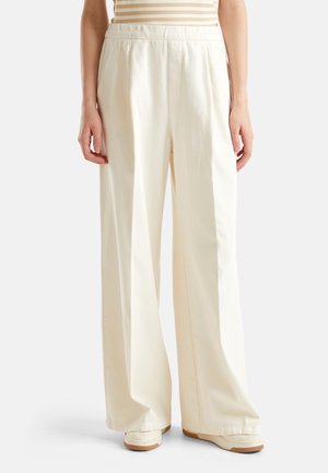 Mujer con pantalones de cintura alta y pierna ancha de color crema y zapatos beige, de pie frente a un fondo blanco.