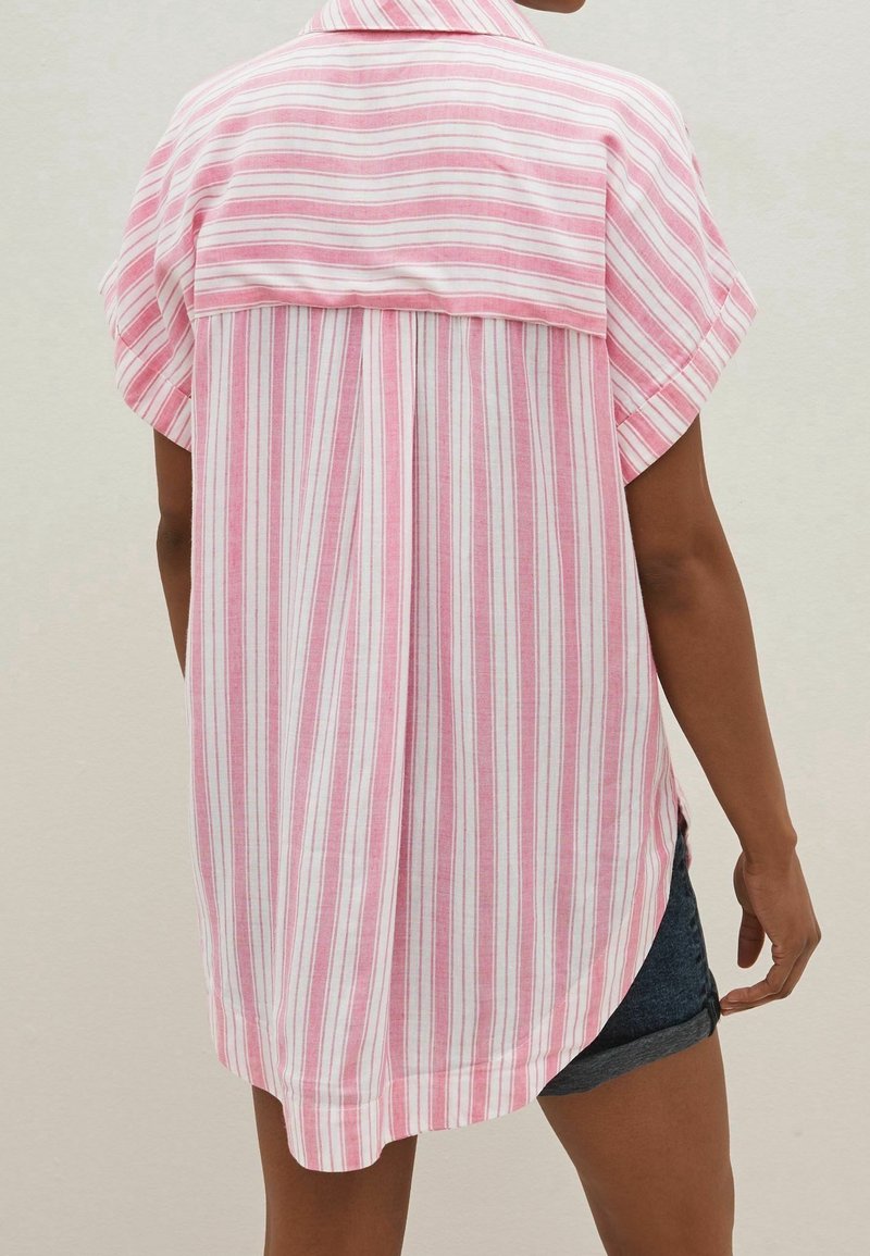 Chemise rayée rose et blanche, manches courtes, col, coupe décontractée, fentes latérales. Le tissu semble doux et léger. Le dos présente un empiècement.