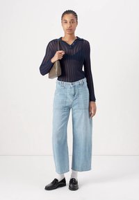 Maglia a maniche lunghe navy con design textures, jeans a gamba larga azzurri chiari e scarpe in pelle nera, mentre tiene una piccola borsa grigia.