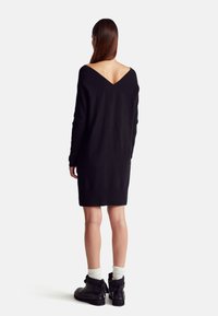 Czarna dzianinowa sukienka z tylu w kształcie litery V, żebrowane detale na ramionach i długie rękawy, zestawiona z czarnymi botkami i białymi skarpetkami.