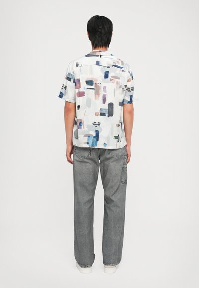 Kortermet skjorte i lett stoff med et fargerikt abstrakt mønster; paret med løse grå jeans og hvite joggesko.