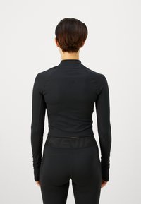 Schwarzes langärmliges Sportshirt mit taillierter Passform, glatter Textur und hohem Kragen, kombiniert mit passenden schwarzen High-Waist-Leggings.