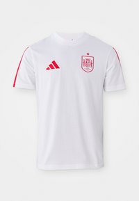 Λευκή ποδοσφαιρική φανέλα της Adidas με κόκκινες λεπτομέρειες, διαθέτει στρογγυλή λαιμόκοψη, κοντά μανίκια και το λογότυπο της ισπανικής εθνικής ομάδας στο στήθος.