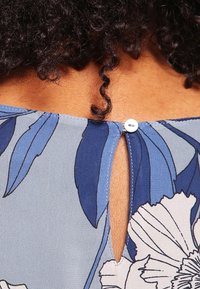 Blue floral patterned fabric with a keyhole back design, featuring a white button closure and smooth texture.