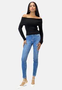 Schwarzer, gerippter Off-Shoulder-Pullover kombiniert mit hellblauen Skinny Jeans und weißen spitzen Ballerinas. Einfaches, tailliertes Design.