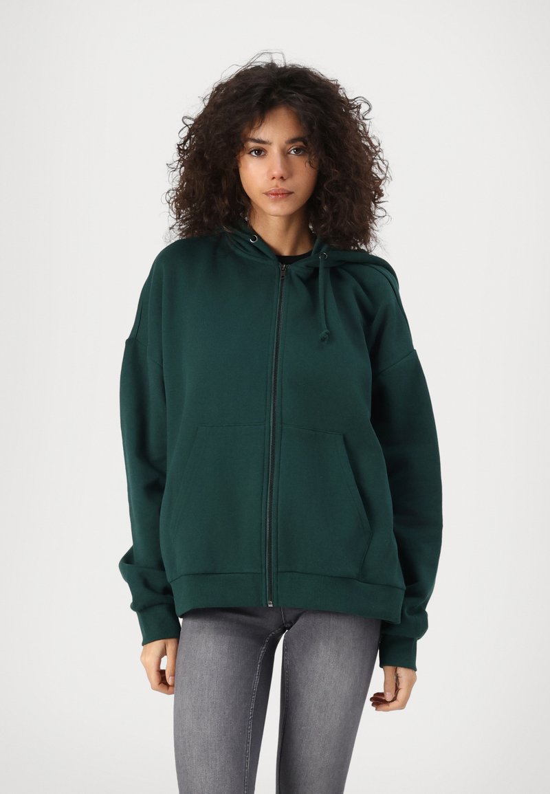 Zelena zip-up majica od mekog materijala, s kenguretorom, kapuljačom na vezanje i rebrastim rukavima. Nosio se s uskim sivim trapericama.