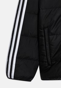 La manica della giacca a vento nera presenta tre strisce bianche lungo il lato, con una tasca visibile e un tessuto liscio e testurizzato.