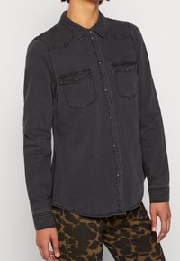 Grijze denimoverhemd met een puntkraag, twee borstzakken en drukknoopsluitingen; lange mouwen met gestikte manchetten en een gebogen zoom.