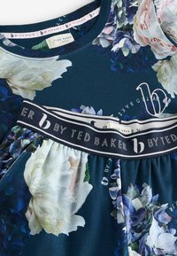 Kleid mit Blumenmuster auf dunkelblauem Hintergrund, mit einem schwarzen elastischen Taillenband, auf dem "by Ted Baker" in weißer Schrift steht, und einem gerafften Rock.