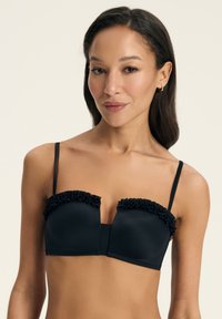 Czarny biustonosz braletka z falbaną wzdłuż górnej krawędzi, wykonany z miękkiego materiału, z usztywnianymi miseczkami i cienkimi regulowanymi ramiączkami. Prosty i uporządkowany design.