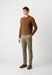 Smeđi dlakavi pulover, uske khaki hlače i smeđe cipele. Outfit sadrži okrugli izrez i rebraste manžetne na puloveru.